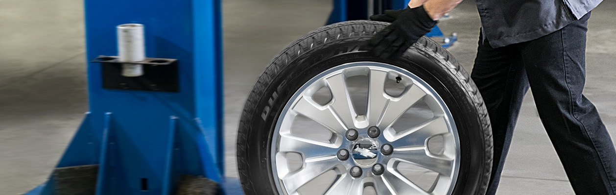 Waist-down shot of a mechanic rolling a tire with large rims across a service garage